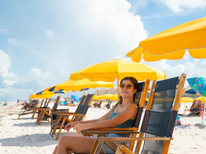 a woman relaxes in a beach chair under a yellow umbrella at Palm Pavilion Inn on Clearwater Beach