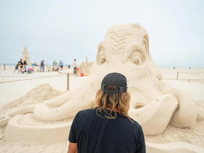 a person looks at a giant sand sculpture of an octopus at Sanding Ovations Master's Cup