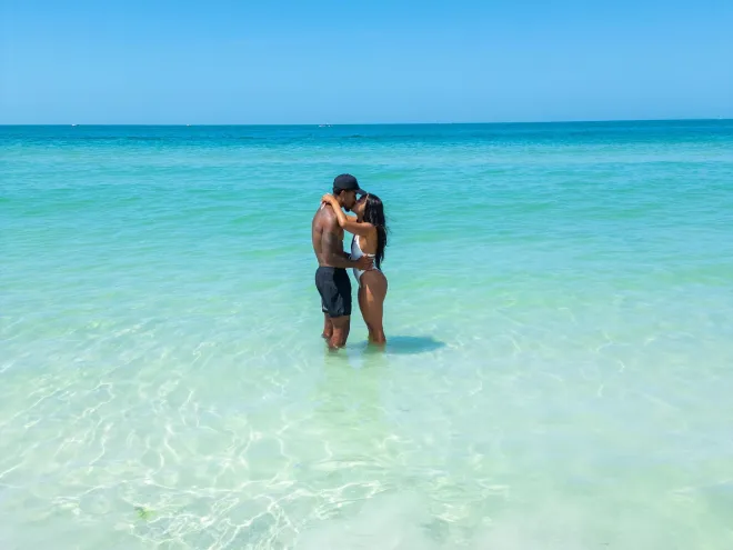 a couple kissing while standing in clear turquoise waters at the beach