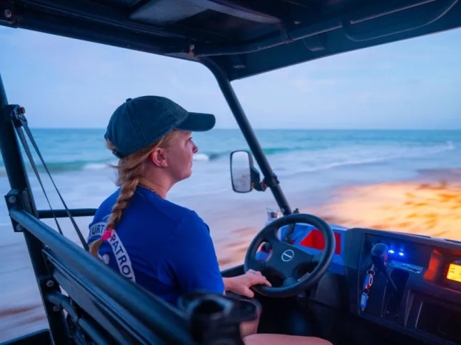 Woman driving an ATV on the beach during sunrise.