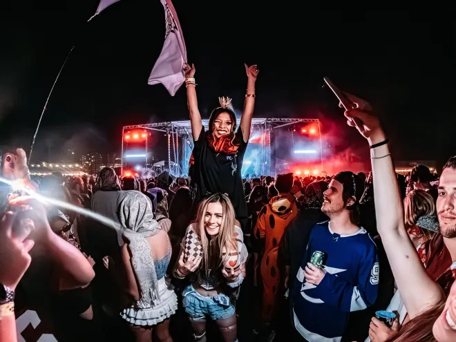 Two women cheer in a lively crowd at Haunted Fest in St. Pete, with one sitting on the other's shoulders.