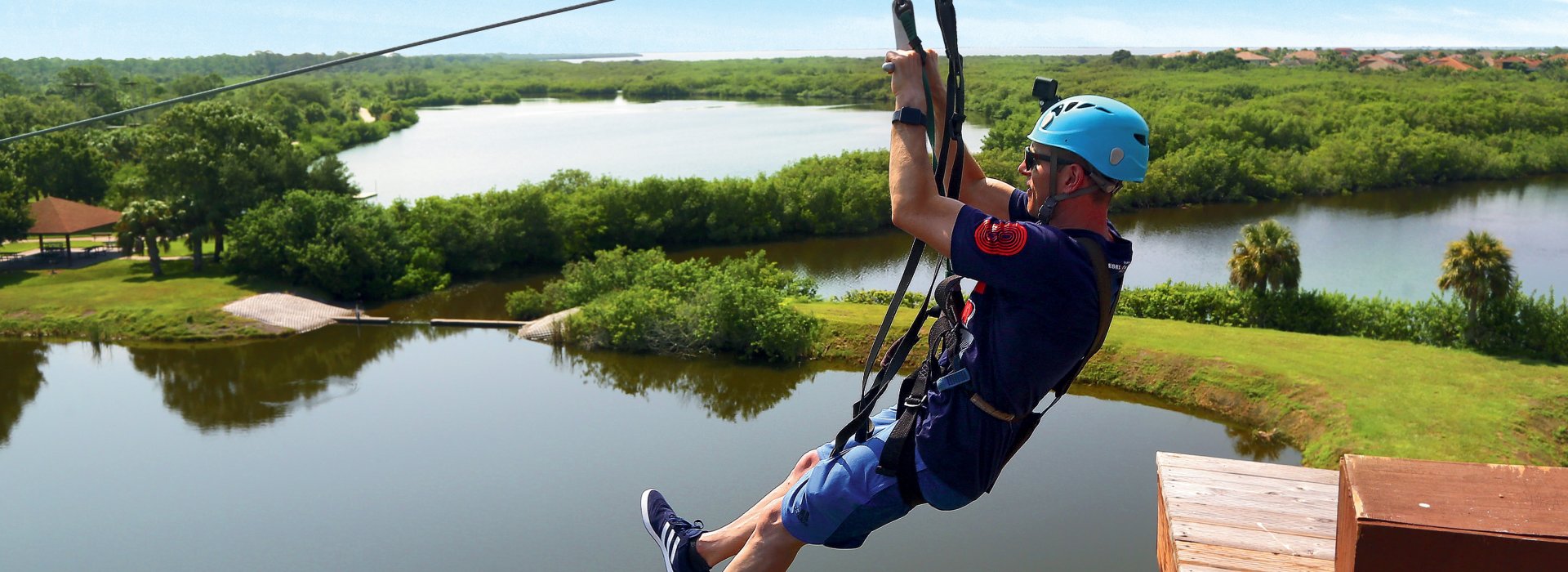a man ziplines above Mobbly Bayou Wilderness Preserve in Oldsmar; a lake and trees can be seen below him