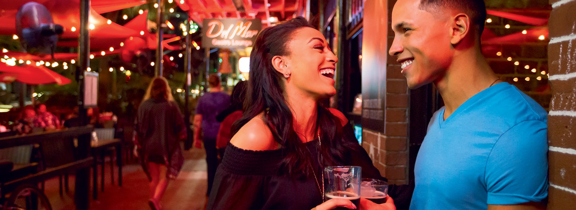 A couple enjoying drinks while standing against the brick facade of Del Mar Lounge in St. Pete.