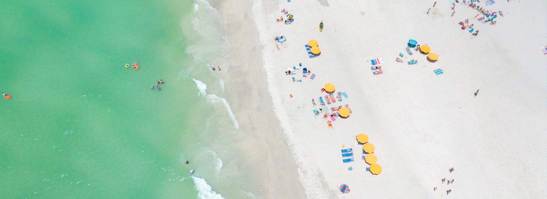 Aerial view of yellow beach cabanas and emerald-green waters of Treasure Island.