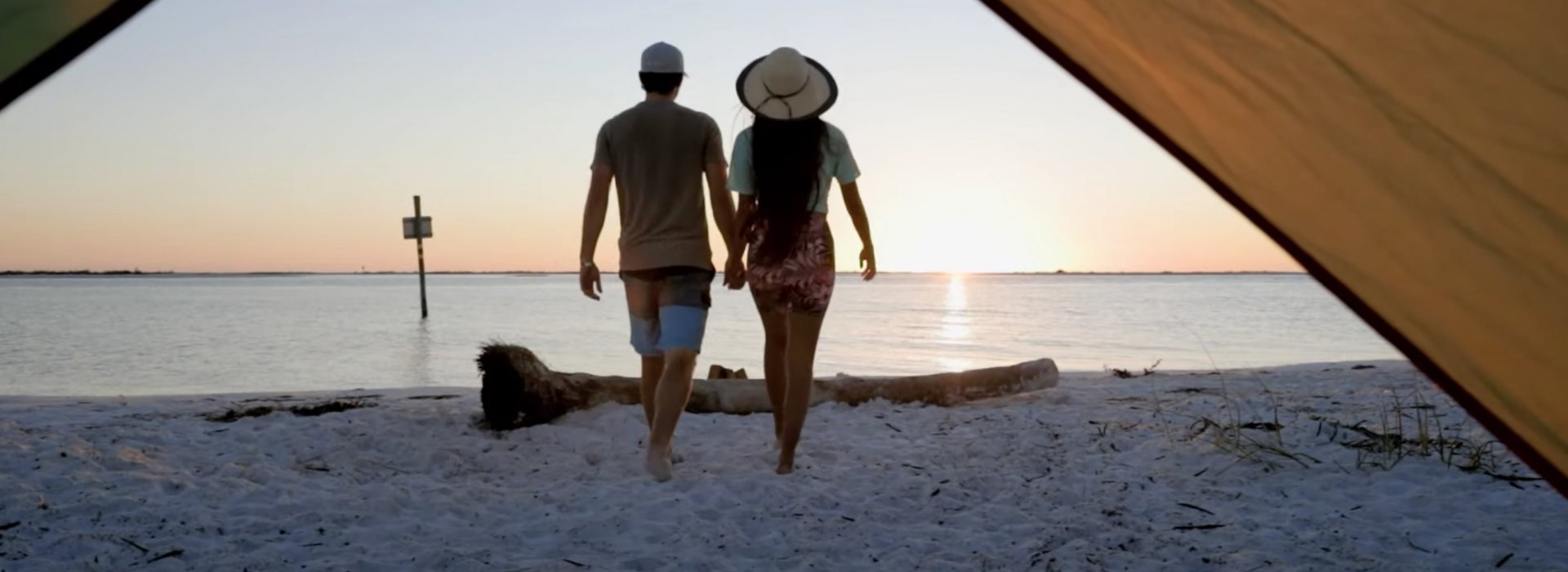 A couple walks away from a tent toward the water at Shell Key during sunset