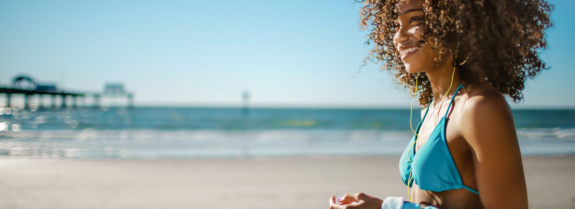 A woman on Clearwater Beach stands and smiles away from camera with Pier 60 in the background