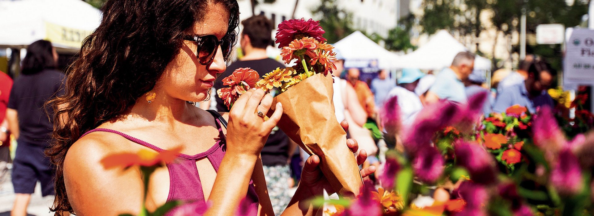 A young lady wearing sunglasses smelling flowers on display.