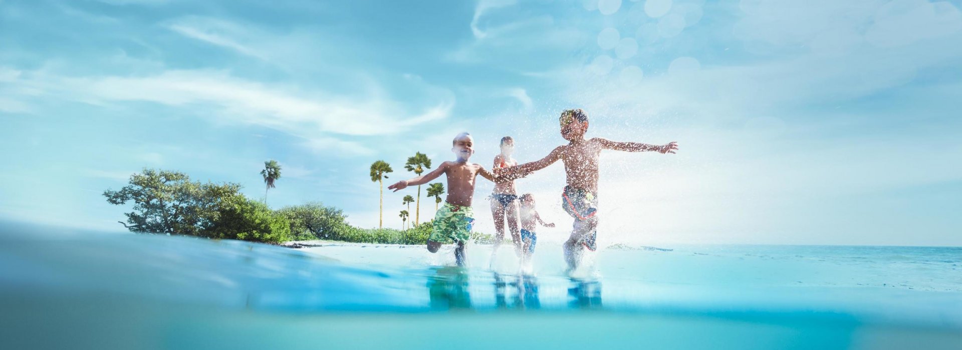 Three children play in the ocean in front of an island.