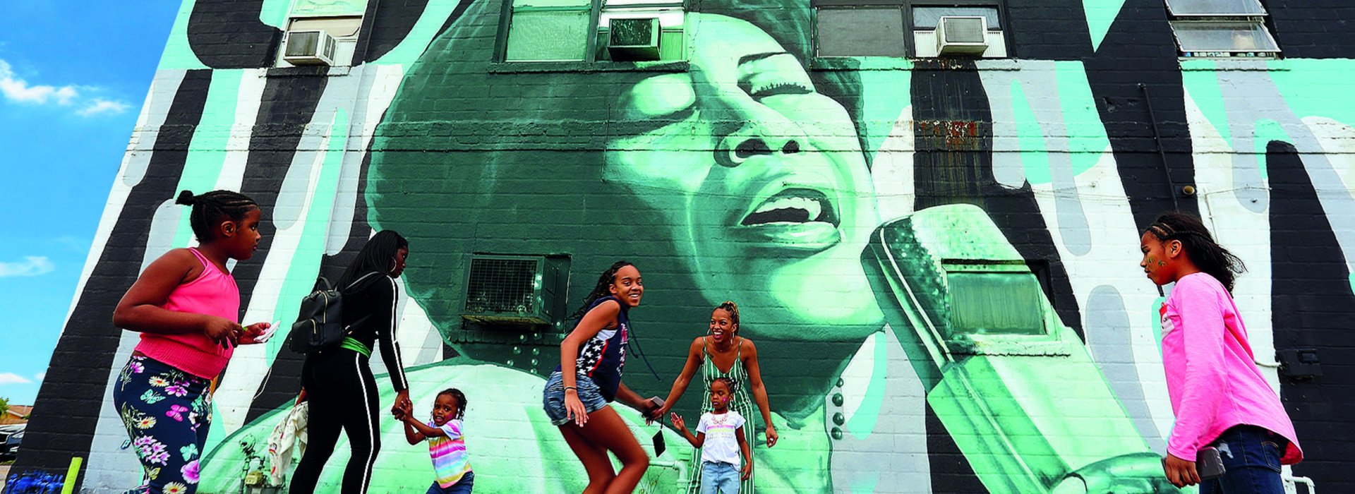 Children and parents playing outside in front of a wall mural in the Deuces Live district during the day.