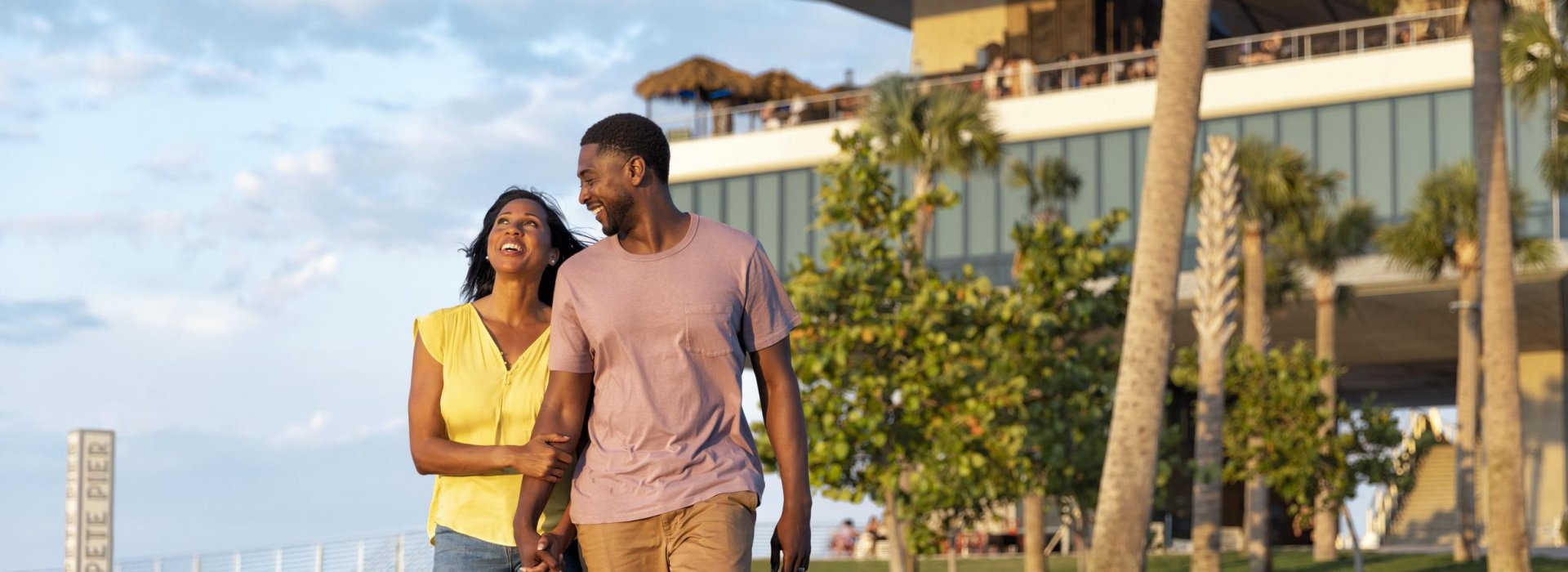 Couple holding hands in front of St. Pete Pier building