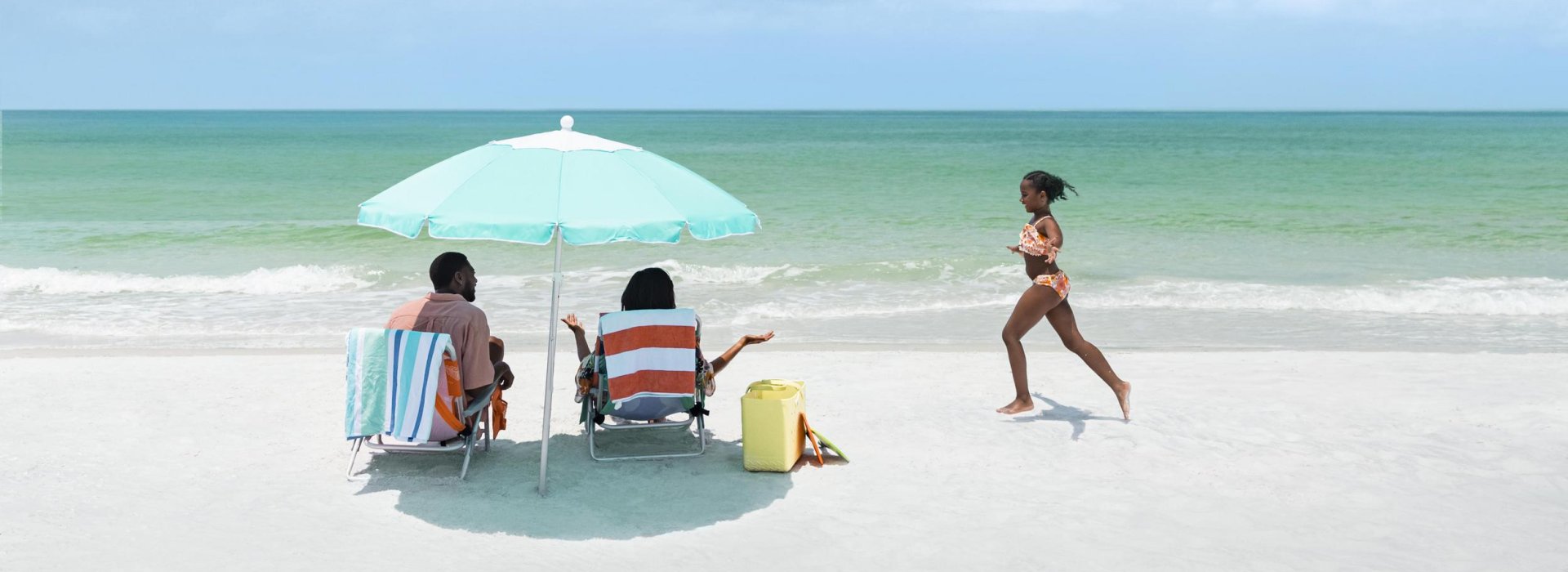 Girl running on the beach toward parents under an umbrella