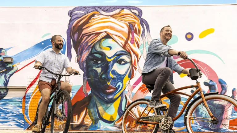 two men riding bikes in front of a mural of an African woman with a turban
