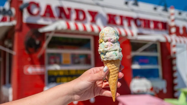 a person's hand holding a stacked ice cream cone in front of the nostalgic red and white Candy Kitchen in Madeira Beach