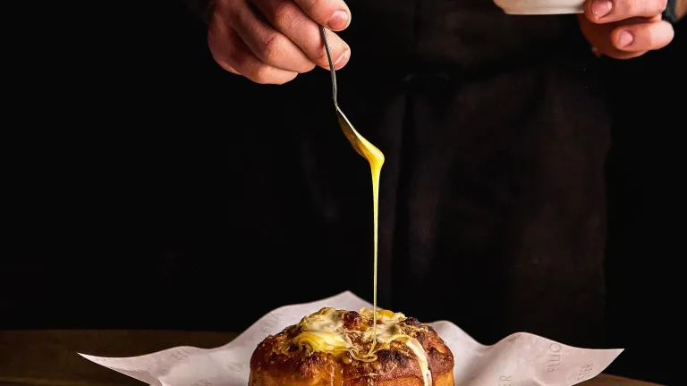 a chef drizzling a bechamel sauce on top of a popover