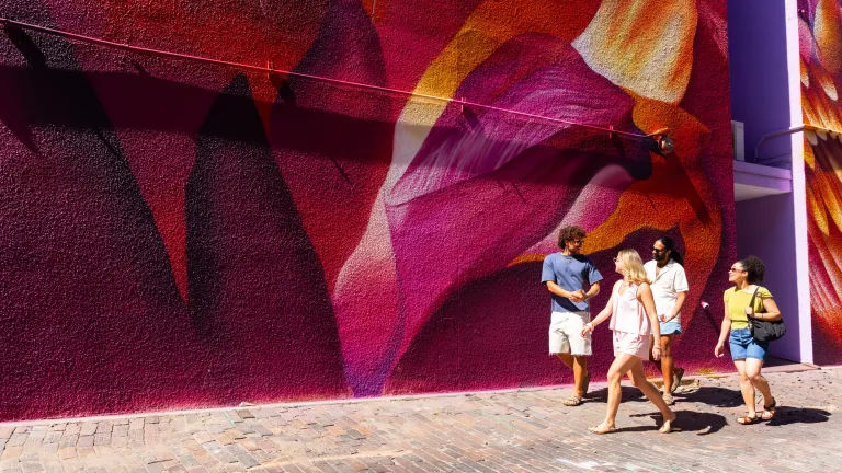 four young people walk past a colorful mural in St. Pete