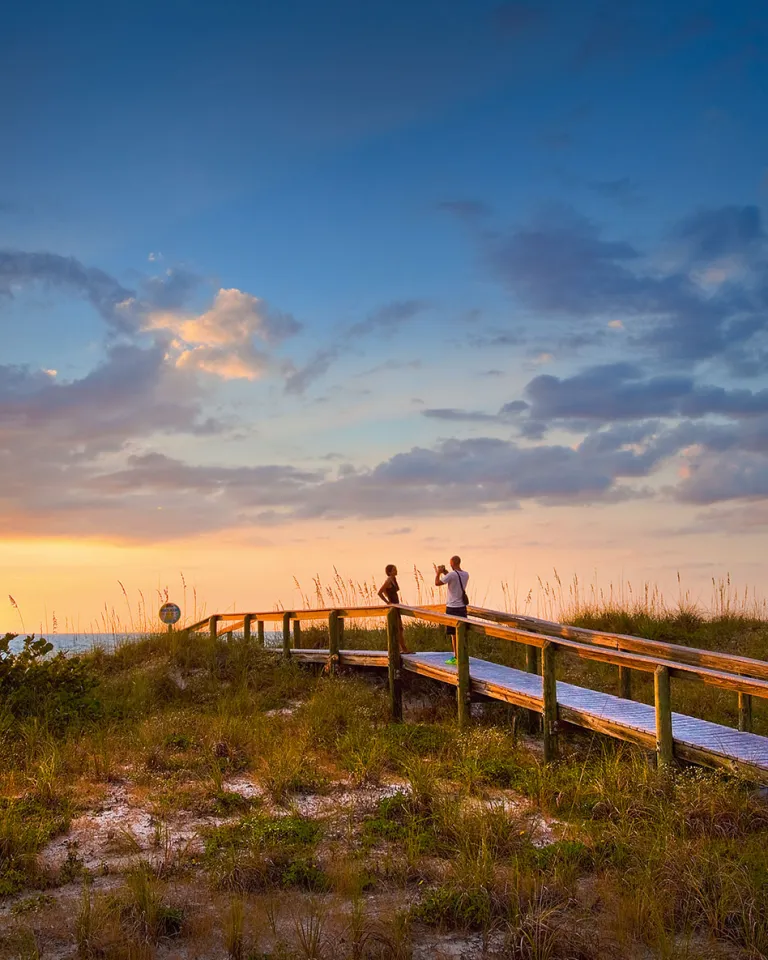 A couple taking photos during sunset at a beach walkway on beautiful Pass-a-Grille Beach near St. Pete Beach, Florida