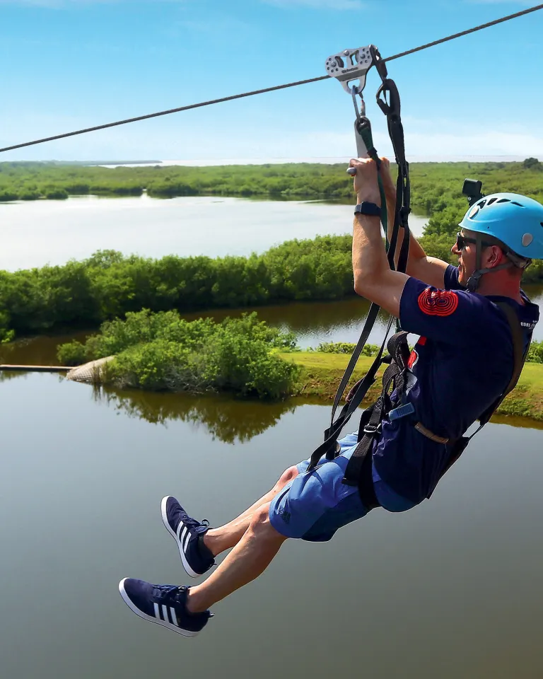 a man ziplines above Mobbly Bayou Wilderness Preserve in Oldsmar; a lake and trees can be seen below him