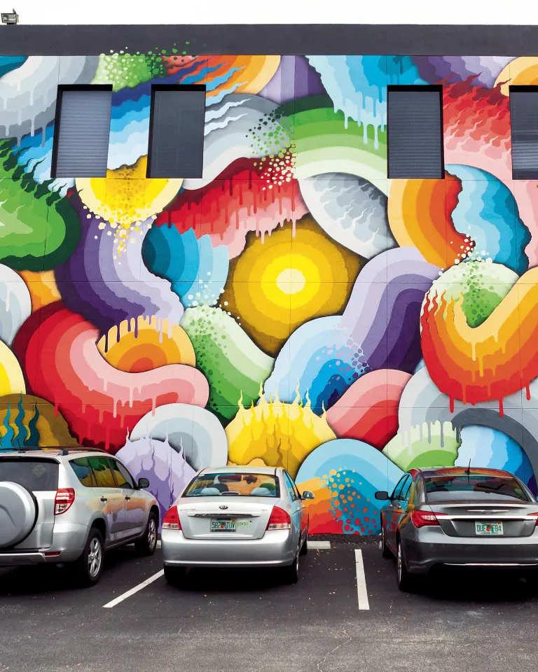 Several cars parked in front of a colorful mural