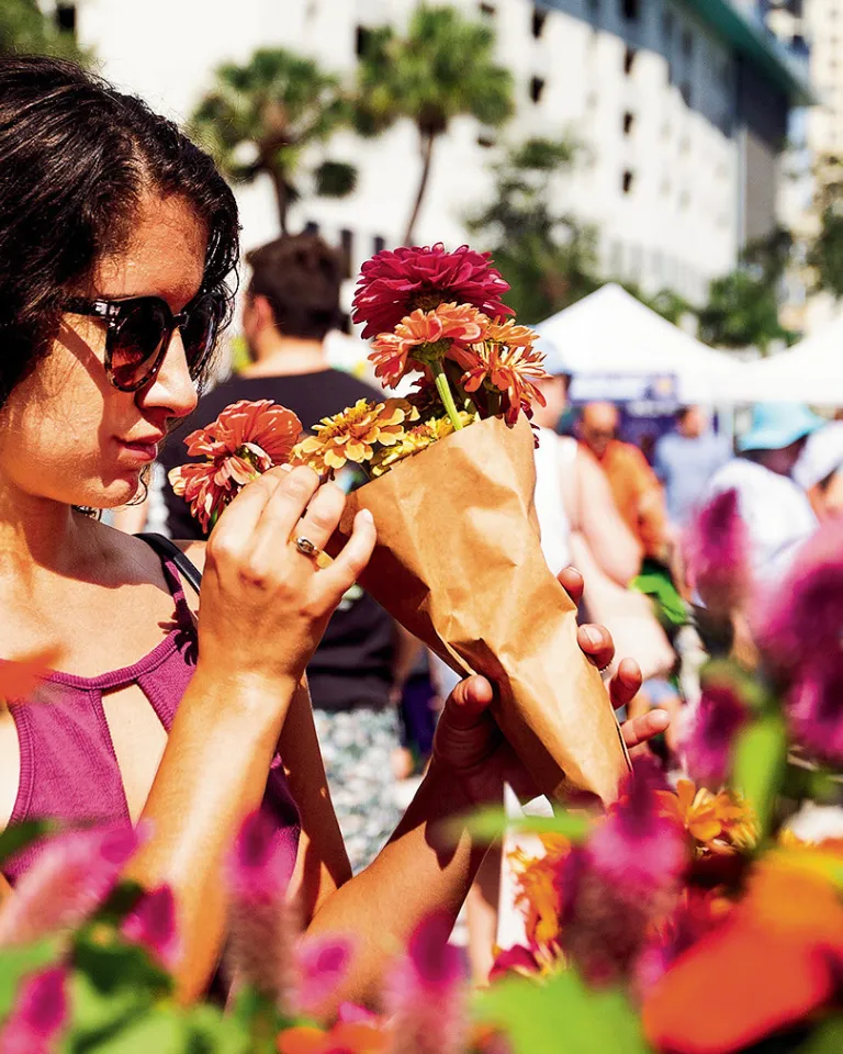 A young lady wearing sunglasses smelling flowers on display.