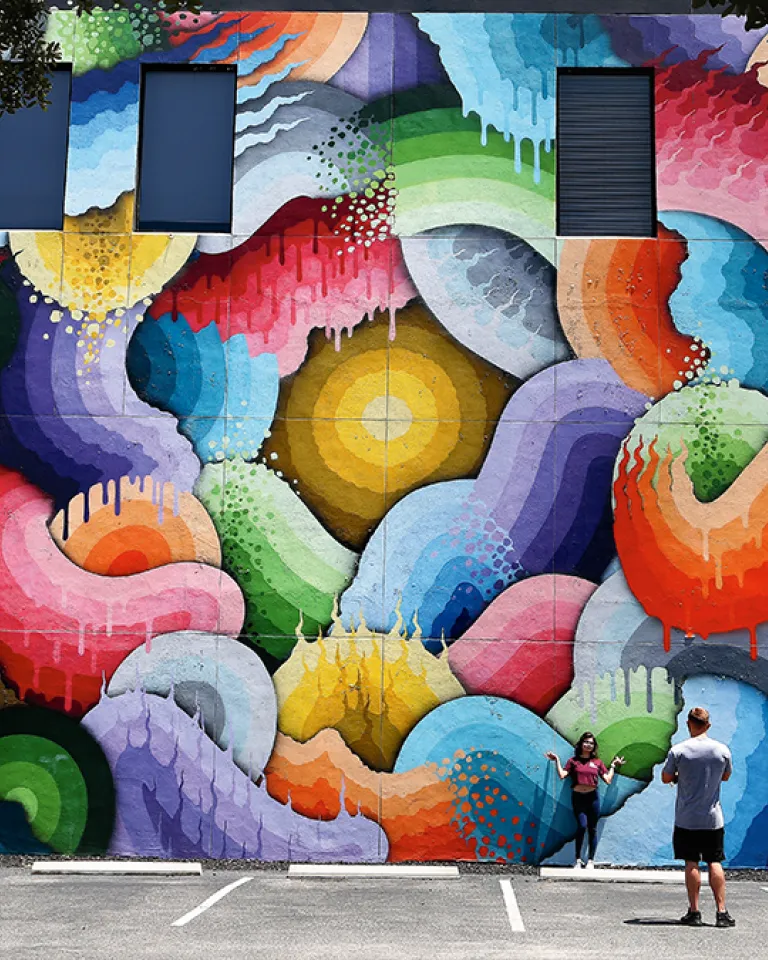 A couple taking a photo in front of the Space Rainbows mural