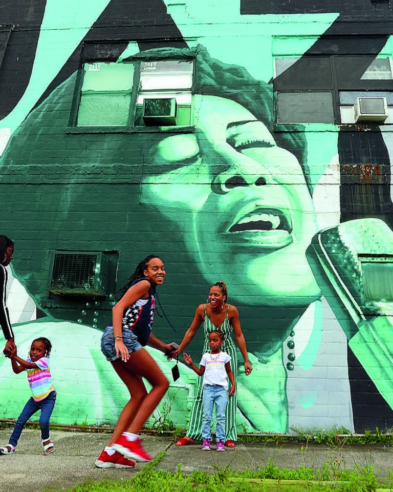 Children and parents playing outside in front of a wall mural in the Deuces Live district during the day.