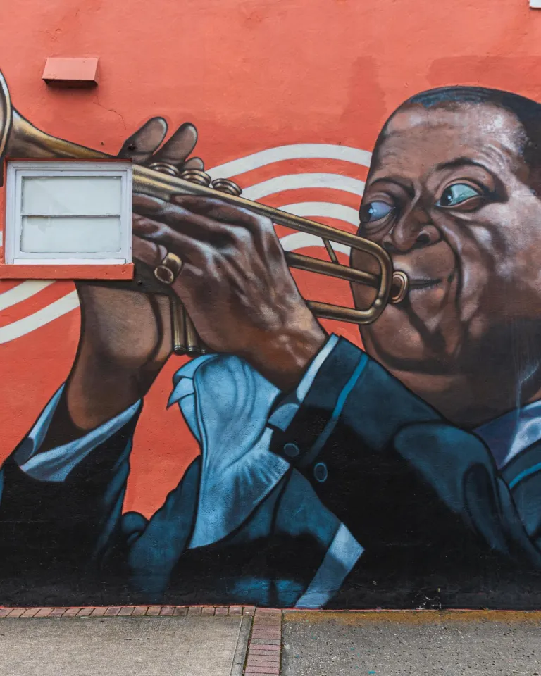 A mural by Herbert Davis in South St. Pete on a red background depicts Louis Armstrong playing the trumpet