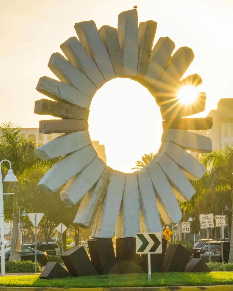 The sun rises behind a stone sun sculpture in Saint Pete's Edge District.