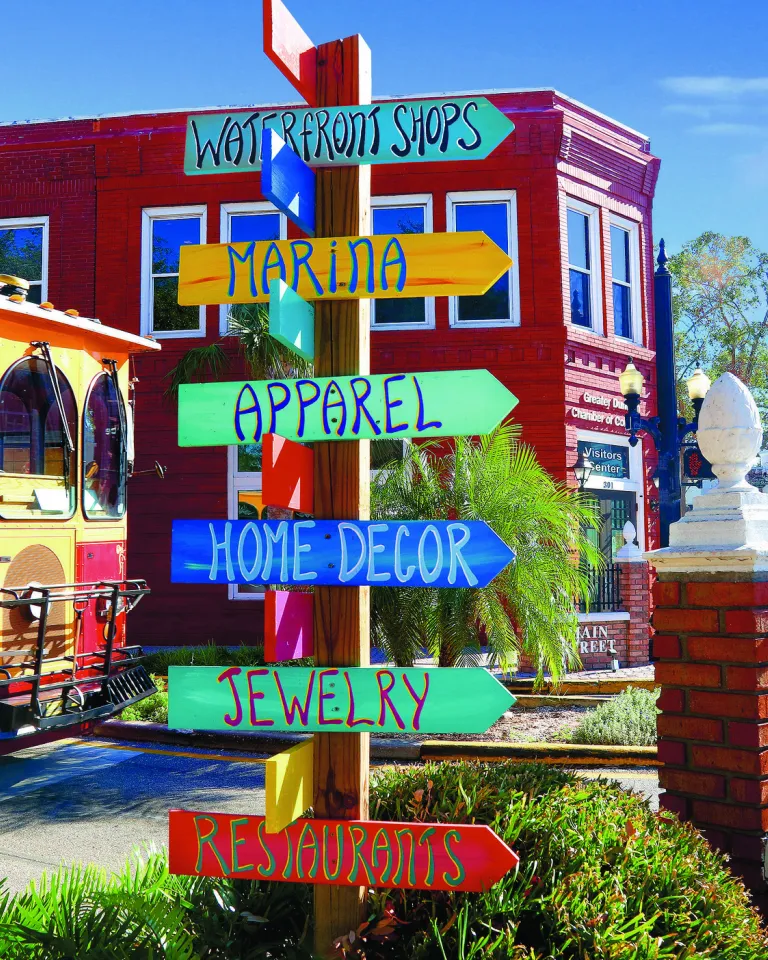 A colorful direction sign is in front of a trolley and shops.