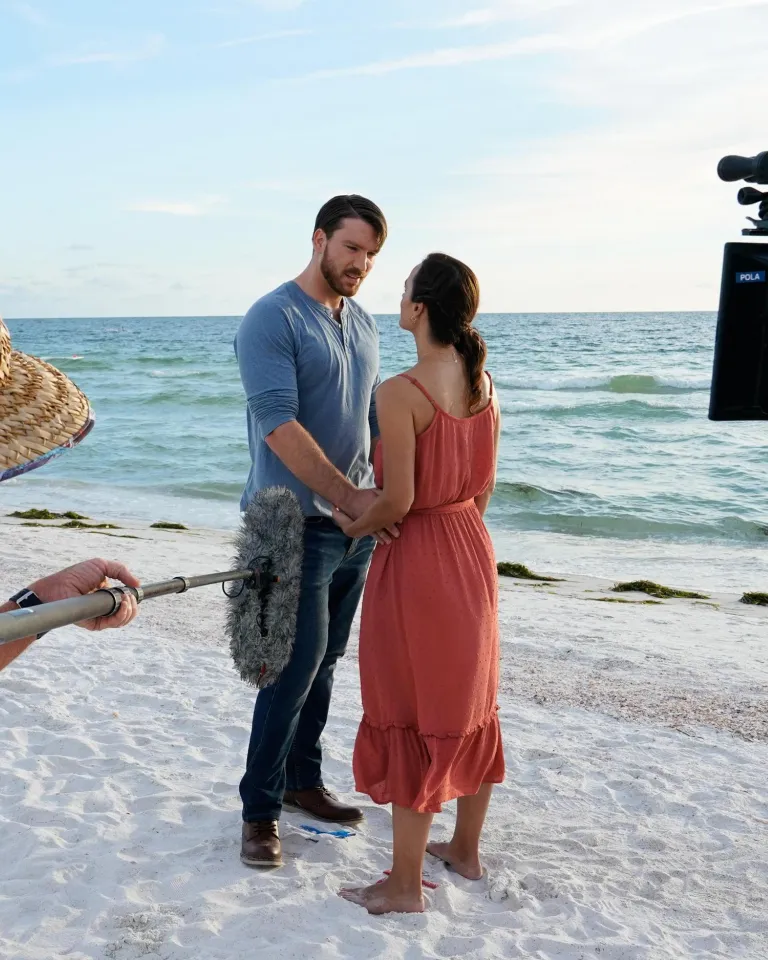 two actors hold hands on the beach while a crew films them for A Taste of Love, a Hallmark movie