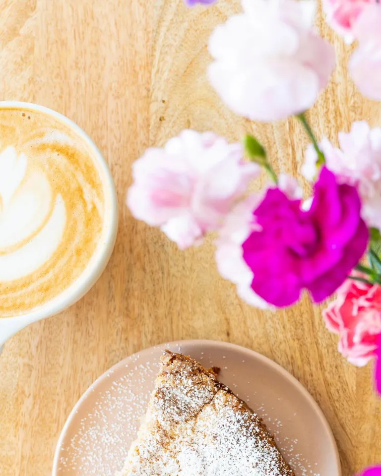 latte in a ceramic mug with a pastry and bright pink flowers