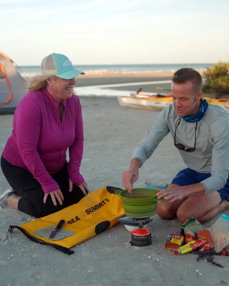 man and woman cooking food on the beach