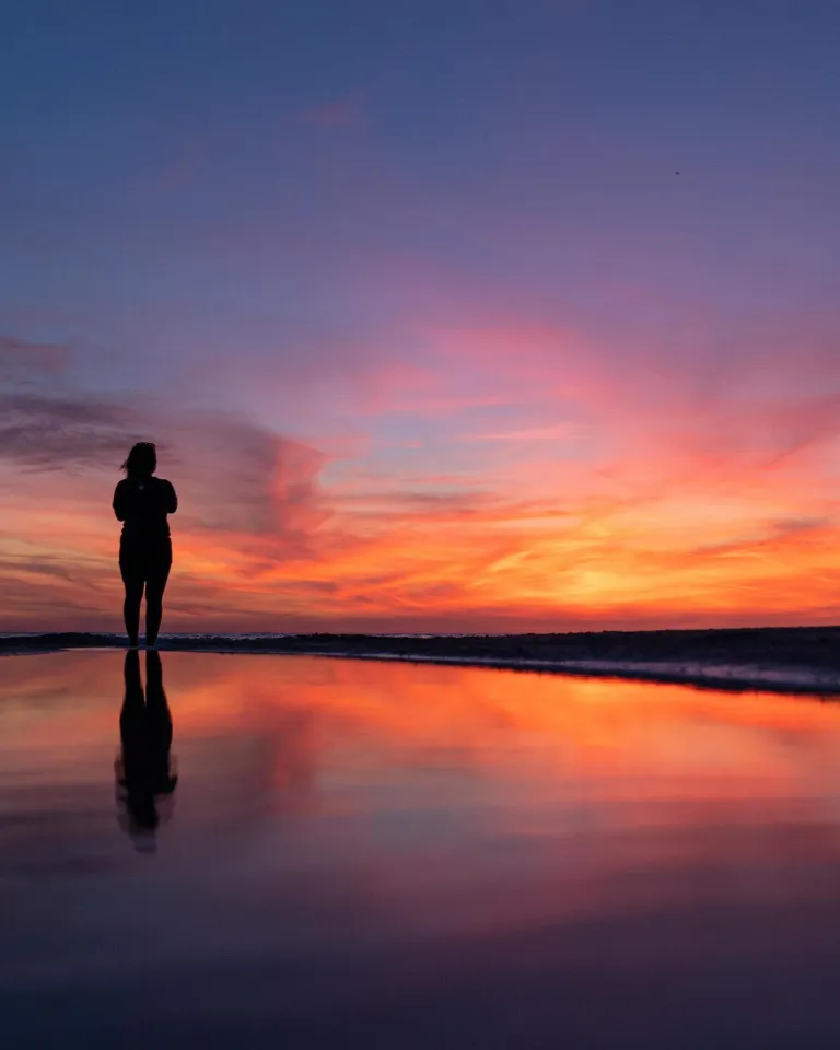 a woman stands on the beach and watches a brilliant sunset in St. Pete-Clearwater
