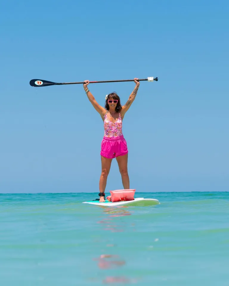 a woman standing up on a paddleboard holding her paddle over her head at Pass-a-Grille Beach