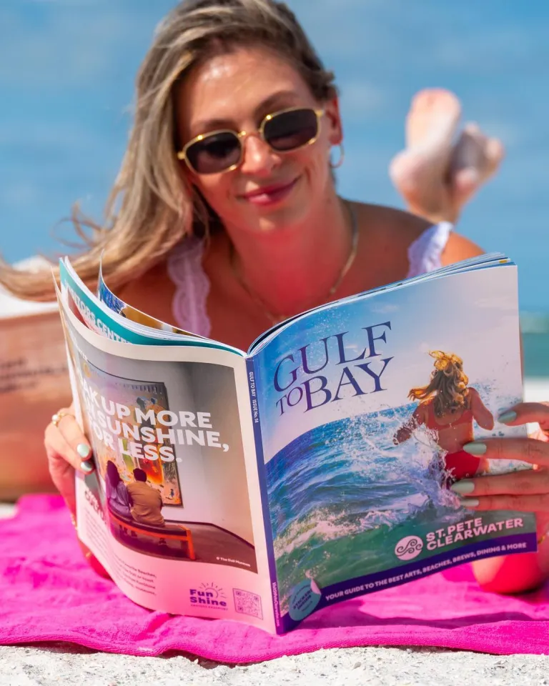a woman reading a Gulf to Bay magazine at the beach