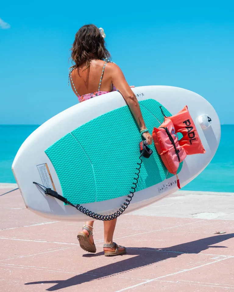 A woman walks toward the beach from Paradise Grill holding a paddleboard rental
