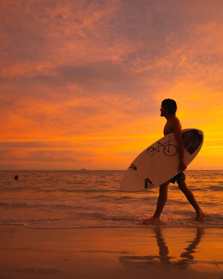 A man walks by the beach at sunset holding a wakeboard in Treasure Island