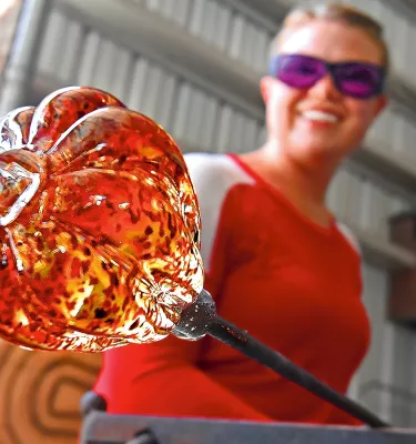 A glass artist holds a piece of glass over heat