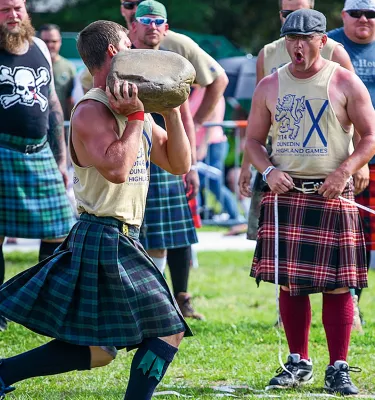 a young man in a kilt throws a rock while the crowd cheers at Dunedin's Highland Games