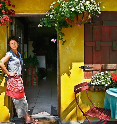 a smiling server waits at the entrance of Pia's Trattoria, a cozy Italian restaurant in Gulfport; the building is painted bright yellow and a table is outside