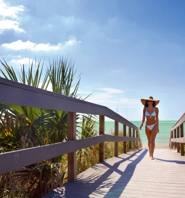 A young woman in white bikini walking off of Indian Rocks Beach.