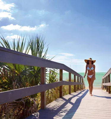 A young woman in white bikini walking off of Indian Rocks Beach.