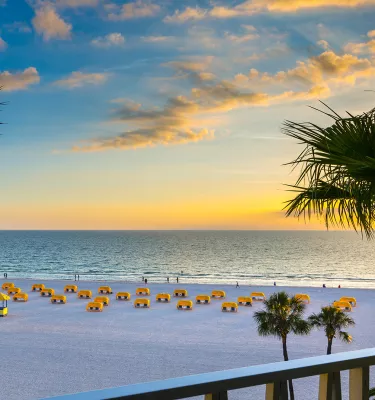 A view of sunset from a balcony at Alden Suites with yellow cabanas on a white sand beach