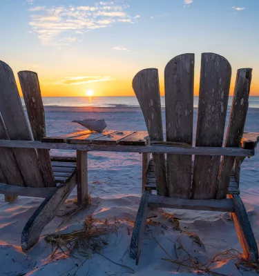 Two Adirondack chairs facing the Gulf waters at sunset in Pass-a-Grille Beach during sunset