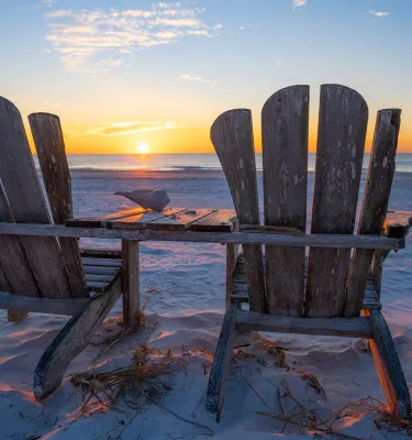 Two Adirondack chairs facing the Gulf waters at sunset in Pass-a-Grille Beach during sunset