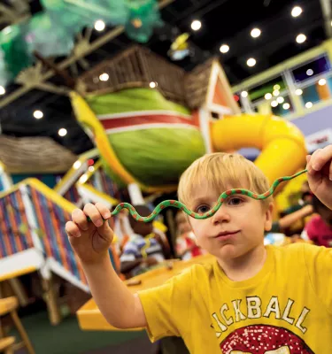 A child holds up a small toy snake at the Great Explorations Children's Museum