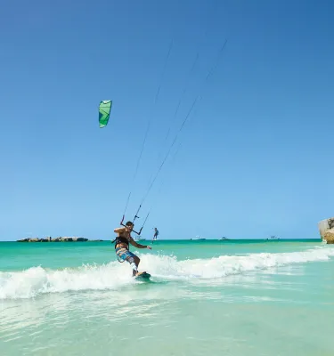 A man kitesurfing off Egmont Key. The water is emerald green with small waves and the ruins of Fort Dade can be seen.