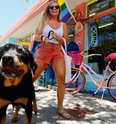 A girl walking a rottweiler in front of a store with an LGBTQ flag and a pink flamingo