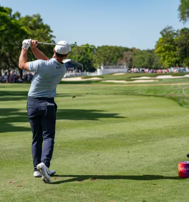 A golfer right after hitting the ball. A large crowd can be seen at a distance.