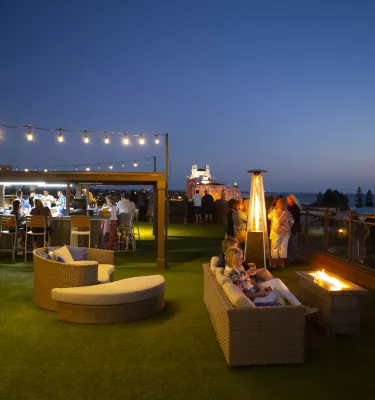 Overview of rooftop bar at Hotel Zamora at dusk showing people enjoying drinks by the fireplace.