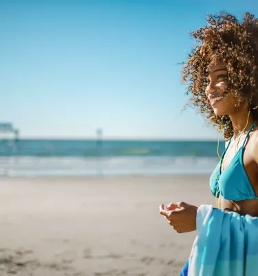 A woman on Clearwater Beach stands and smiles away from camera with Pier 60 in the background